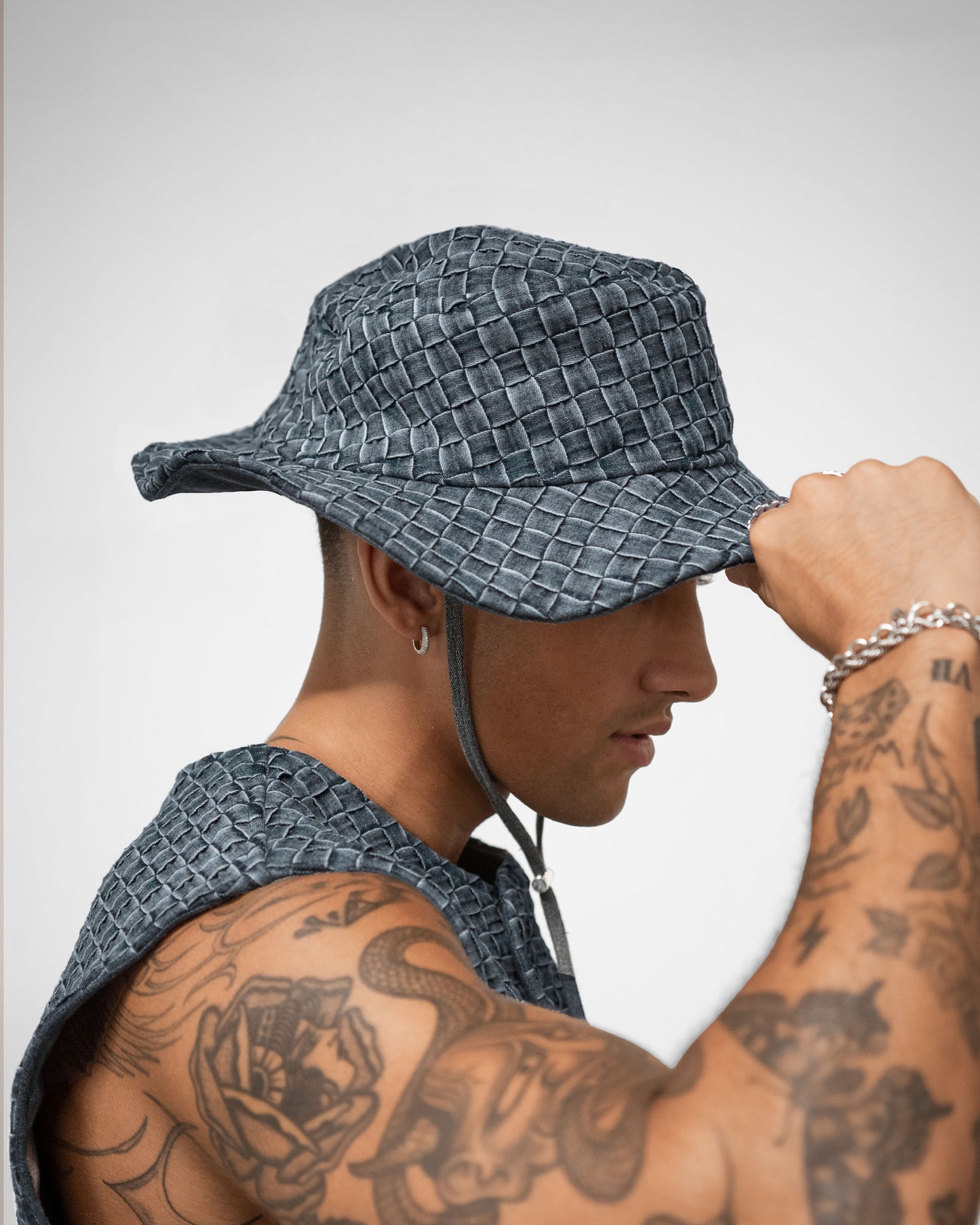 Person wearing a textured blue bucket hat with tattoos on arms against a plain background by BRYDER in London