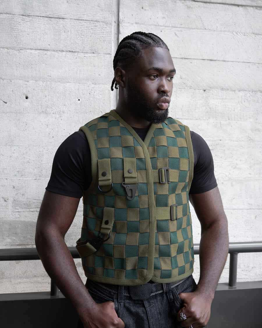 Man wearing a green checkered vest against a concrete wall.