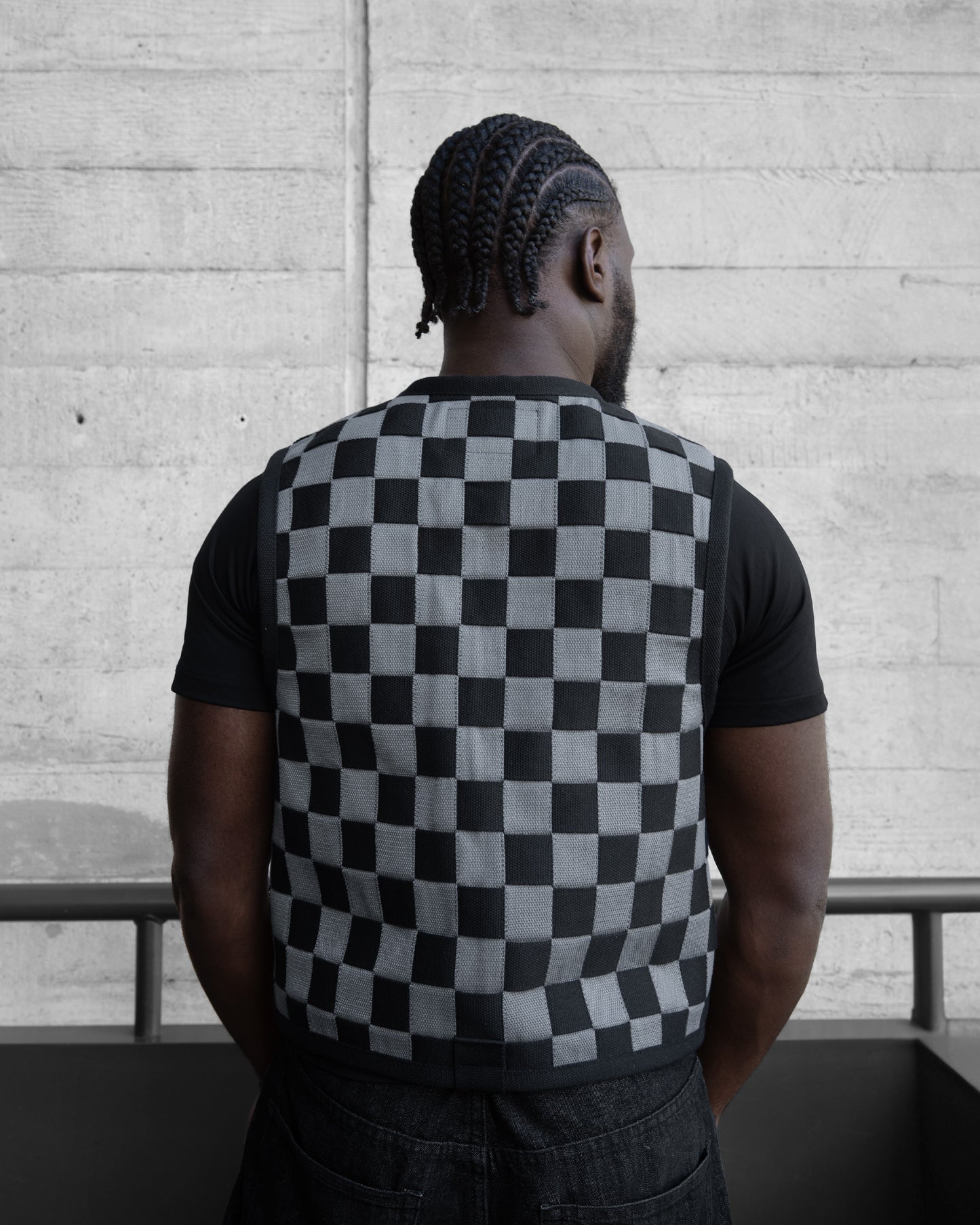 Person wearing a black and white checkered shirt with a concrete wall background