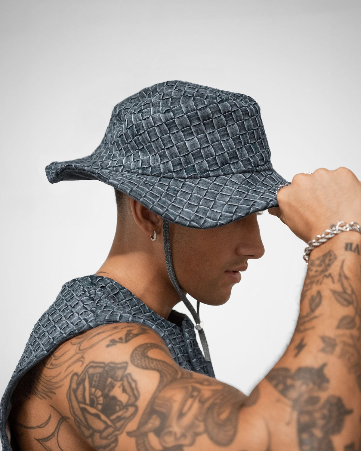 Person wearing a textured blue bucket hat with tattoos on arms against a plain background by BRYDER in London